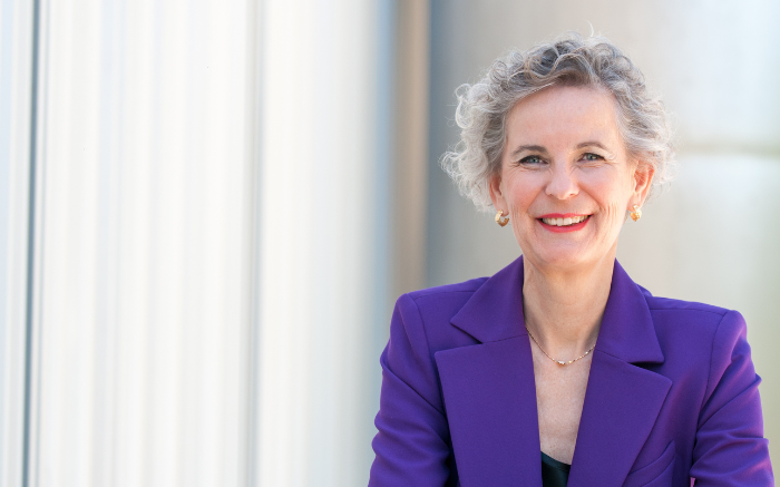 Older woman with short gray hair wearing a purple blazer by a window.
