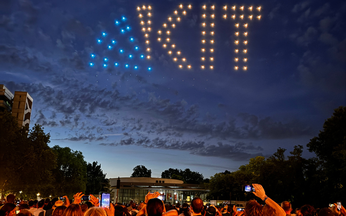 Drone light show displaying "KIT" logo above an audience at dusk outdoors.