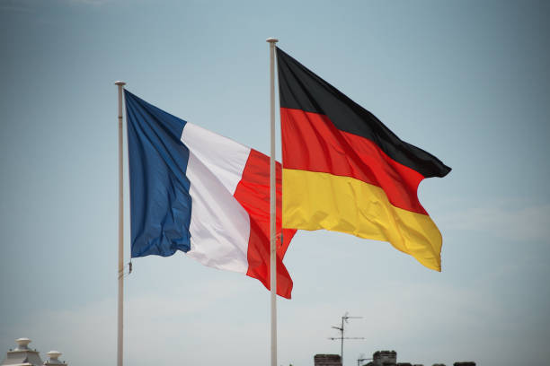 Französische und deutsche Flagge wehen nebeneinander vor blauem Himmel.